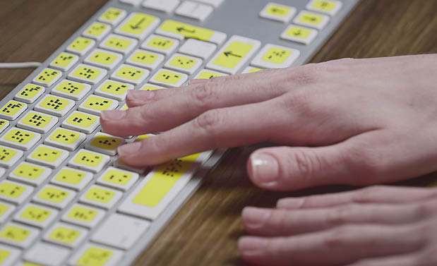 Close-up of a computer keyboard with braille. A blind girl is typing words on the buttons with her hands. Technological device for visually impaired people. Tactilely touches bumps on the keys