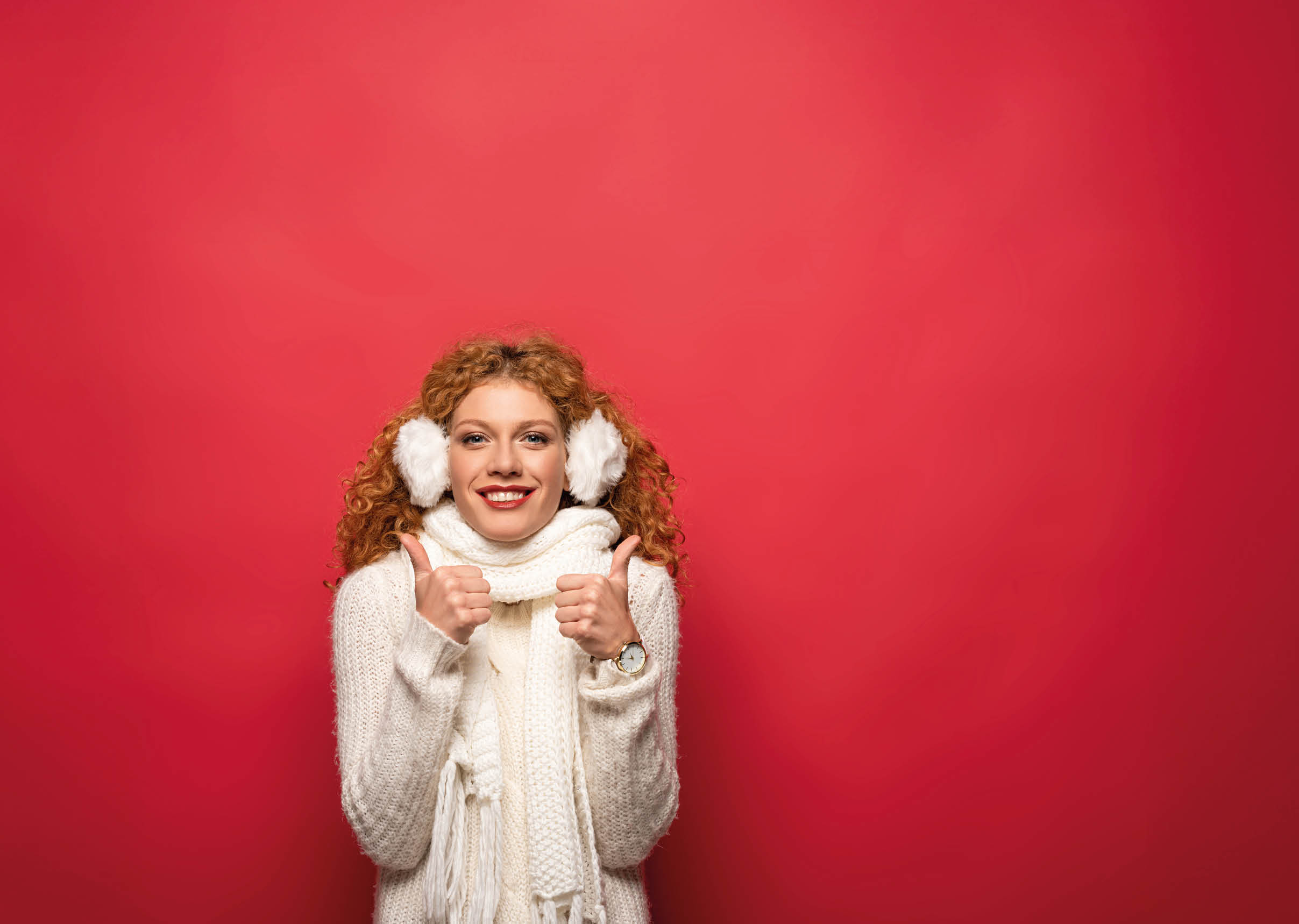 happy woman in winter outfit showing thumbs up isolated on red