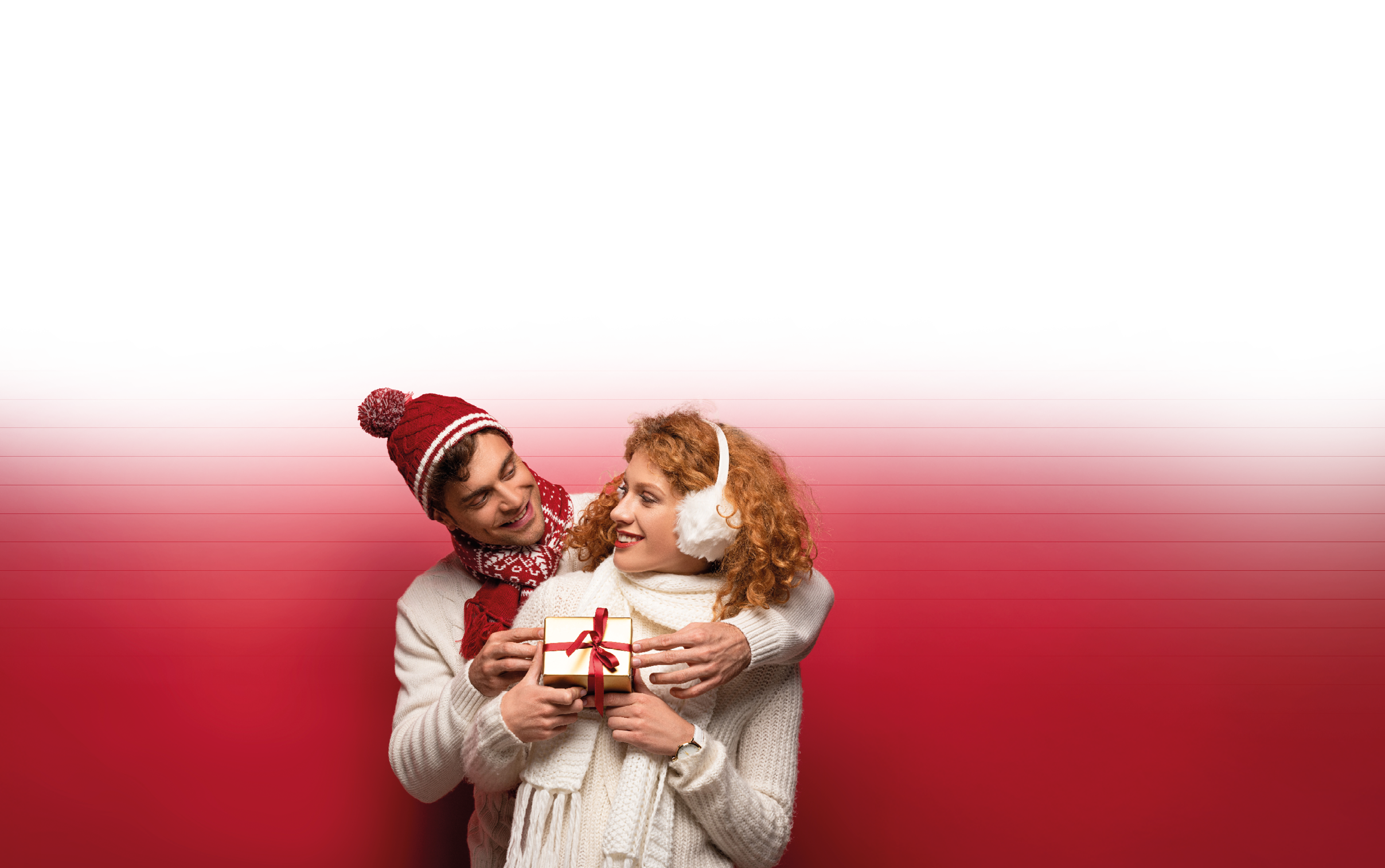 happy couple in winter outfit holding christmas gift isolated on red