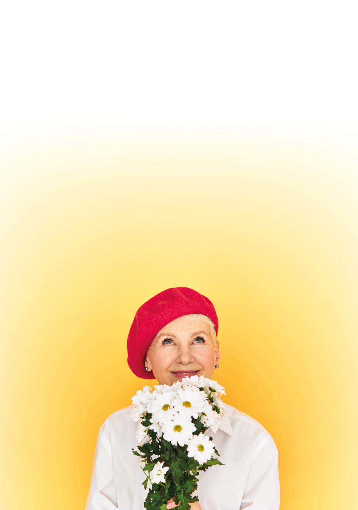 Studio shot of beautiful elegant French woman pensioner in stylish red beret enjoying aroma from white daisies, looking up with happy smile. Spring is in the air. Holidays and special occasions