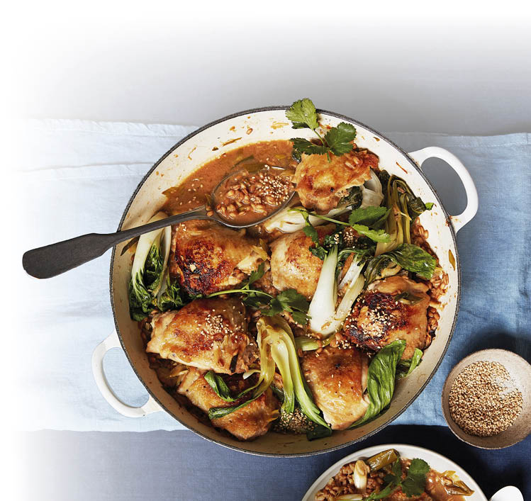 Das Bild zeigt eine runde, helle Auflaufform mit zwei seitlichen Griffen, die auf einem hellblauen Holztisch steht. In der Form liegt ein Ofengericht aus goldbraun gebratenen H hnchenteilen.   Zwischen den H hnchenst cken befindet sich gr nes Gem se, vermutlich Pak Choi, dessen helle Stiele und dunkelgr ne Bl tter gut sichtbar sind. Das Gem se wirkt leicht geschmort und gl nzt von der Sauce.     ber einem der H hnchenst cke liegt ein gro er L ffel, der eine dickfl ssige, braune Sauce mit kleinen K rnern oder Gew rzst ckchen enth lt. Die Oberfl che des H hnchens ist knusprig gebr unt und teilweise leicht karamellisiert.    Die Auflaufform ist fast vollst ndig gef llt, sodass das Gericht  ppig und herzhaft wirkt.    Rechts neben der Form steht ein kleines rundes Gef  , vermutlich mit Sesamk rnern gef llt. Am unteren Bildrand ist au erdem der Rand eines weiteren Tellers zu sehen.