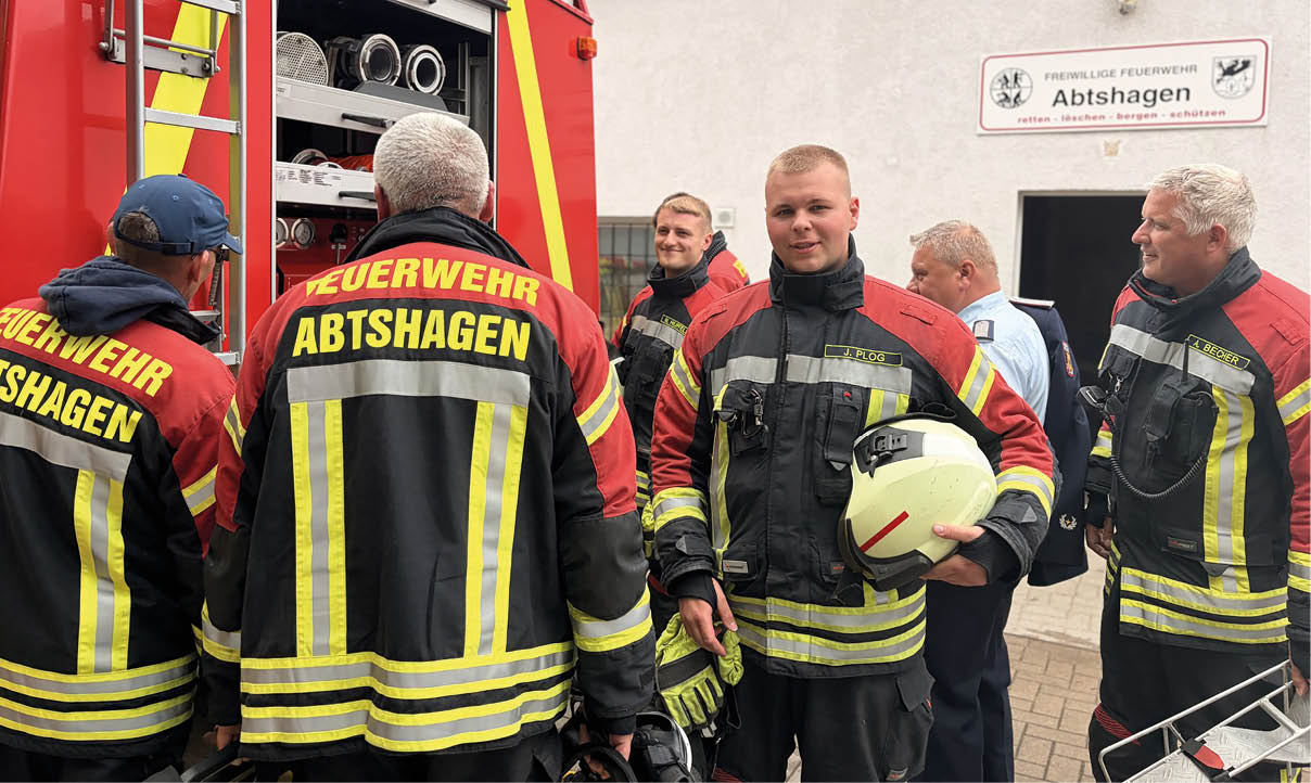 Mehrere Personen in Feuerwehruniformen stehen vor einem ge ffneten Feuerwehrauto und bereiten sich offenbar auf einen Einsatz oder eine bung vor.  Beschreibung von KI generiert