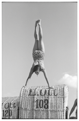 Eine Person tr gt einen gemusterten Badeanzug und macht einen Handstand vor klarem Himmel. Beschreibung von KI generiert