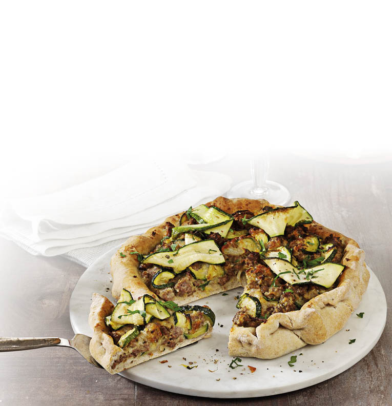 Eine herzhafte Pizza mit Zucchinischeiben und Kr utern liegt auf einem wei en Teller, wobei ein St ck mit einem Messer herausgehoben wird. Beschreibung von KI generiert