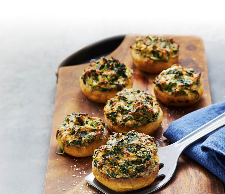 Gef llte Champignons mit Kr utern und K se auf einem Holzbrett mit einem blauen Tuch und einem Metallheber. Beschreibung von KI generiert