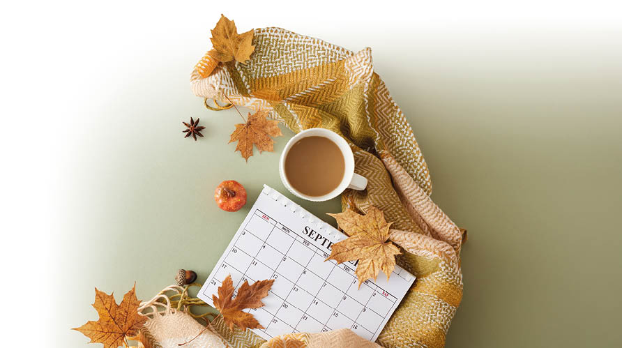 Eine herbstliche Szene mit einem Kalenderblatt f r September, einer Tasse Kaffee, getrockneten Ahornbl ttern, einer kleinen K rbisdekoration und einem gelb-beigen gestrickten Schal auf einem hellgr nen Untergrund. Beschreibung von KI generiert