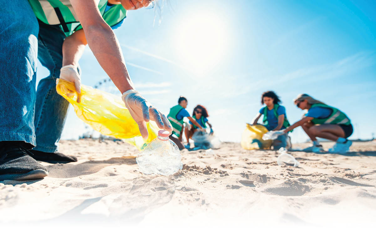 Mehrere Personen in gr nen Westen sammeln bei sonnigem Wetter M ll am Strand und halten dabei gelbe M lls cke. Beschreibung von KI generiert