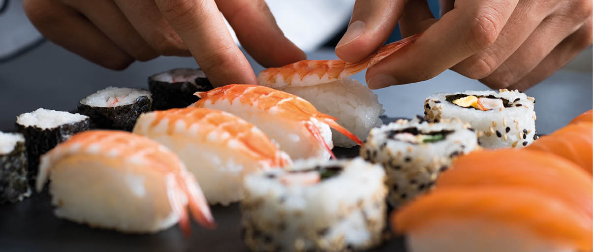 Closeup of chef hands preparing japanese food. Japanese chef making sushi at restaurant. Young chef serving traditional japanese sushi served on a black stone plate.